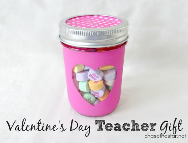 Mason jar teacher gift packed with pens sticky notes and hand cream tied with a Valentine ribbon on a craft table