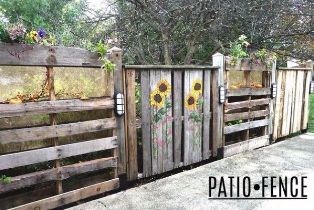 Patio fence, five upright pallets with painted sunflowers, planted top bays, wall lanterns and armrests beside a patio