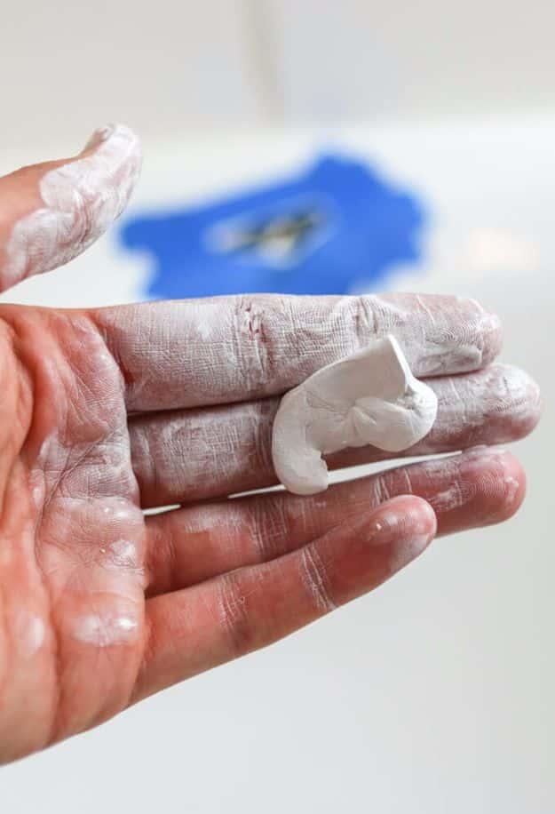 Bathtub chip repair in progress with white two part putty on a fingertip and blue tape masking the tub surface