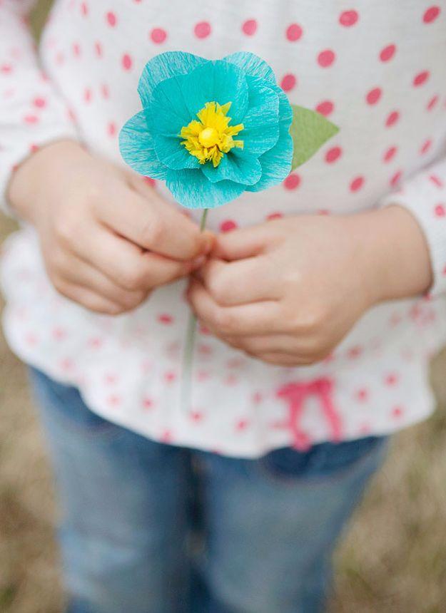 Crepe paper flowers for mom, a turquoise crepe paper flower with a yellow center held by a child in polka dots