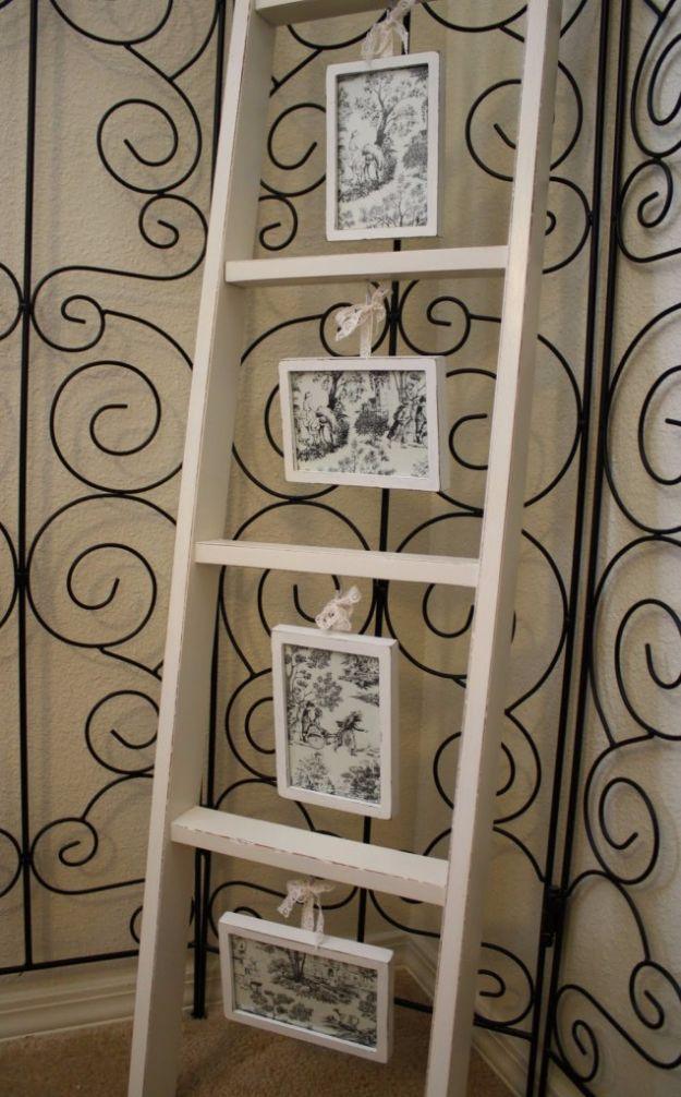Cream painted wooden ladder leaning in a corner with four small framed toile prints hanging from lace ribbons and hooks