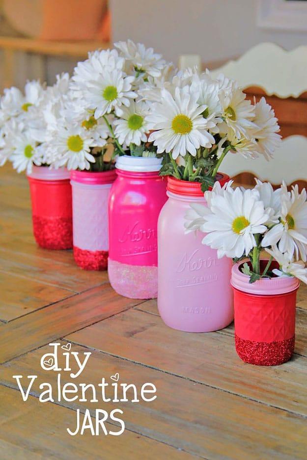 Mason jars dipped in pink glitter with a clean taped line used as vases for carnations, an easy DIY gift to make at home