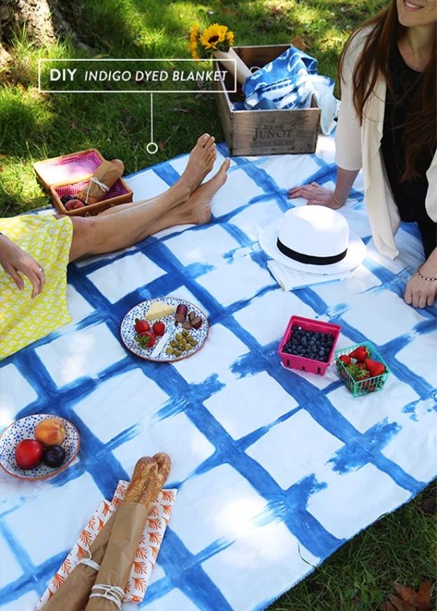 Blue and white indigo dyed cotton blanket spread on grass with fruit, bread, a straw hat and two women
