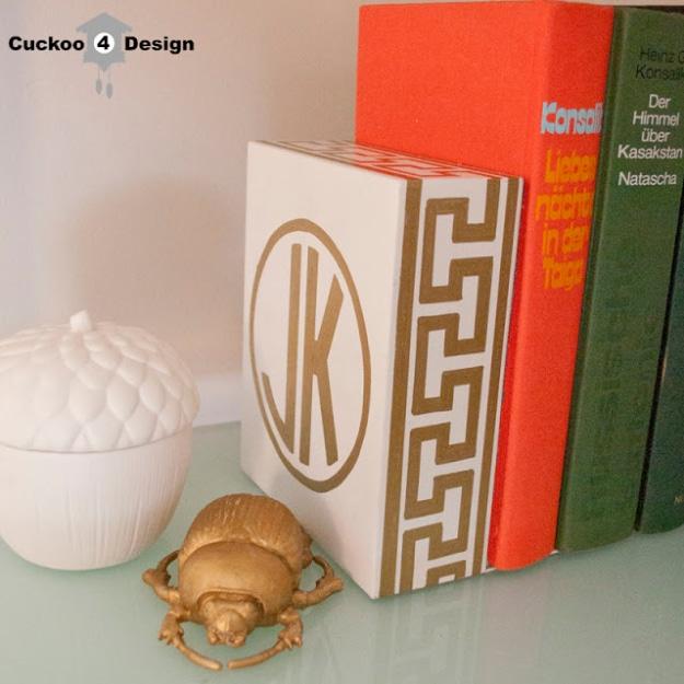 Gold monogrammed greek key bookend, a white bookend drawn with a gold greek key border and circled JK monogram