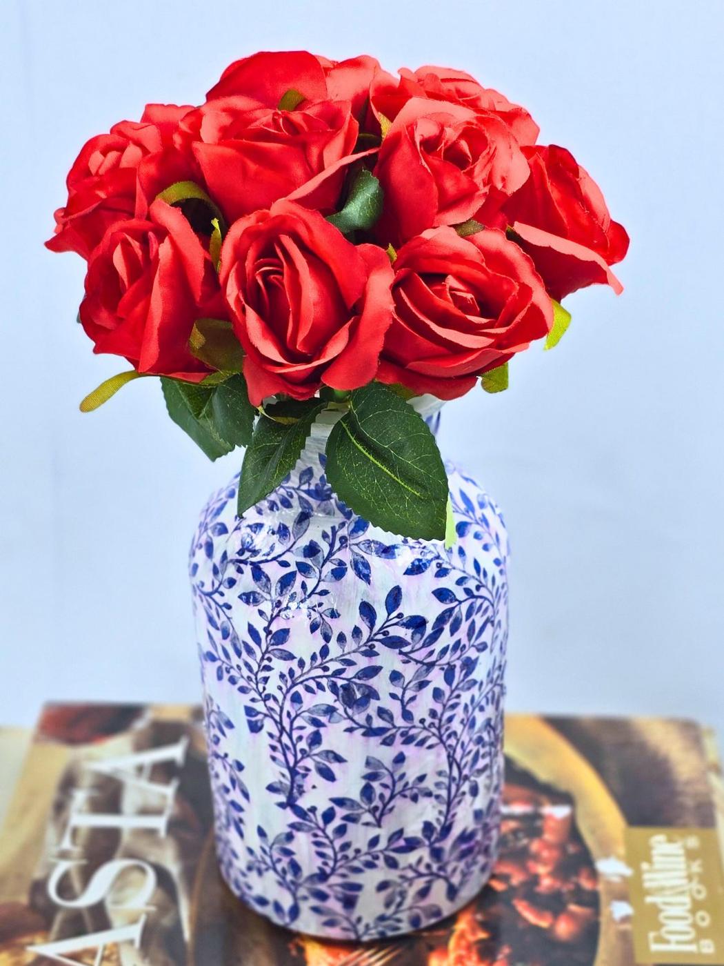 Glass jar decoupaged in a blue and white floral napkin pattern holding a bunch of red roses beside cookbooks