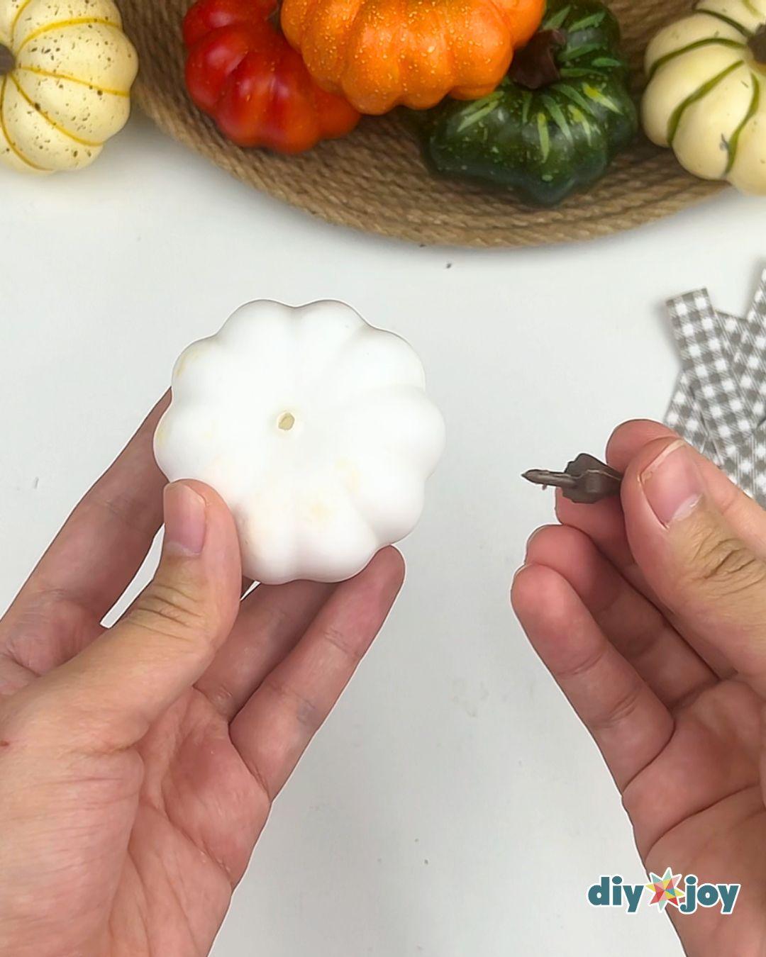 DIY Fall Decor - two hands holding a bare white ribbed faux pumpkin with the stem hole showing and the stem alongside
