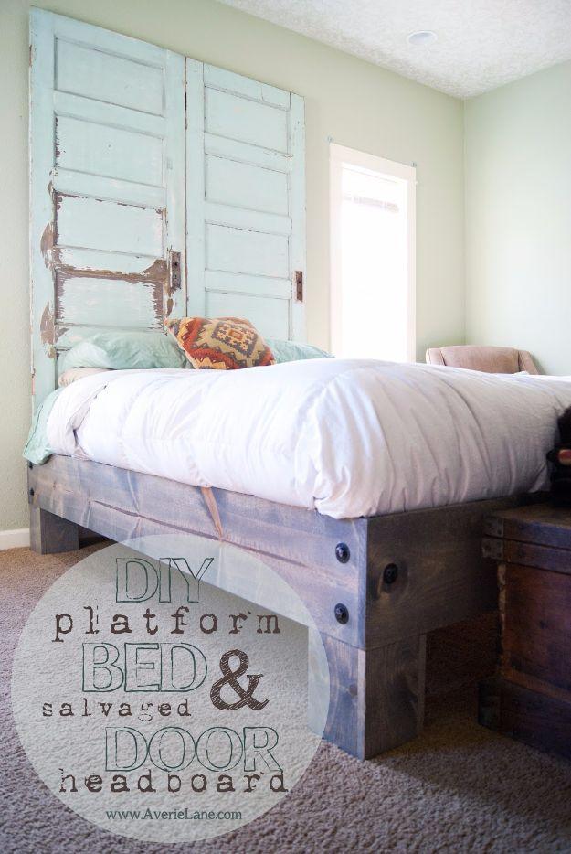 Photograph of a chunky stained wood platform bed with white bedding under two pale green salvaged doors used as a headboard