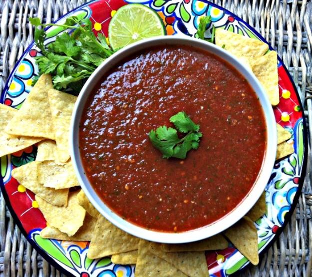 Restaurant style salsa blended smooth in a bowl with cilantro and lime beside a basket of tortilla chips