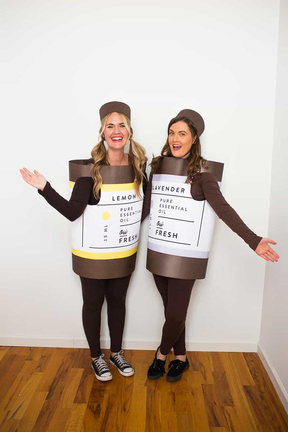 Two women wearing brown essential oil bottle costumes labeled lemon and lavender with matching cap headpieces