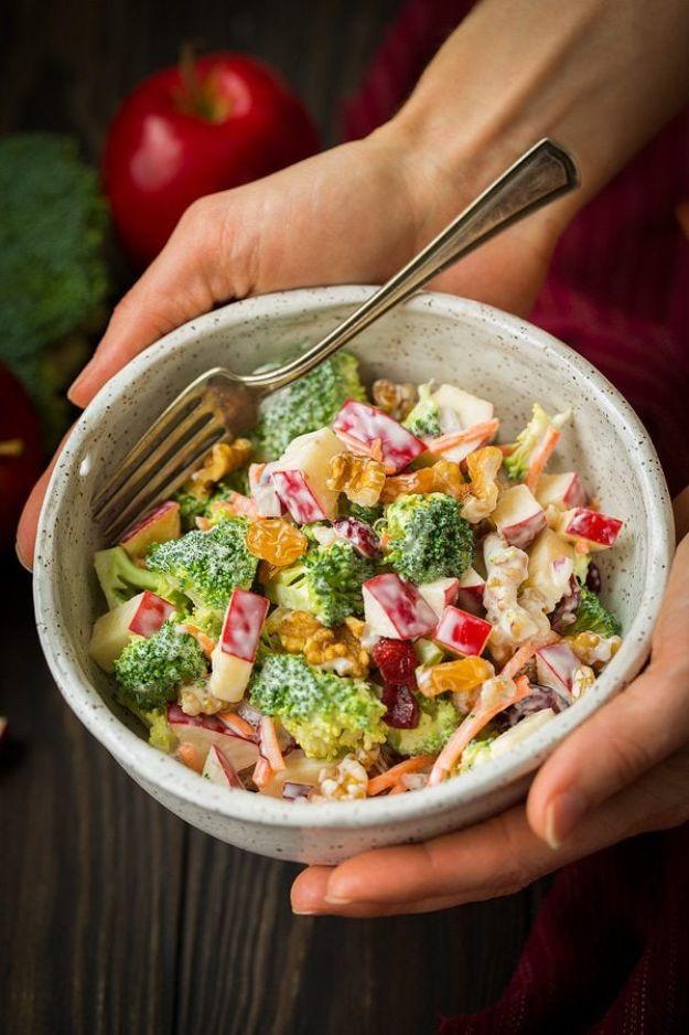 Broccoli apple salad in a stone bowl with diced broccoli, apple, shredded carrot and raisins, held in hands