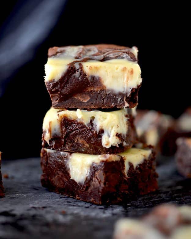 Cheesecake swirl brownies stacked on dark slate with marbled cream cheese ribbons through the chocolate