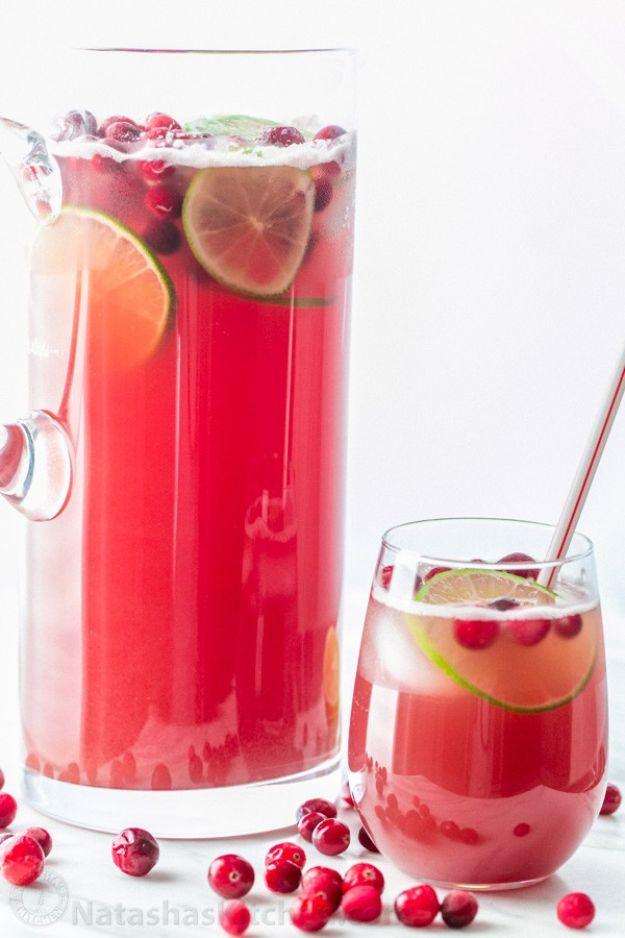 Glass pitcher of red cranberry pineapple punch with lime slices and whole cranberries beside a filled glass