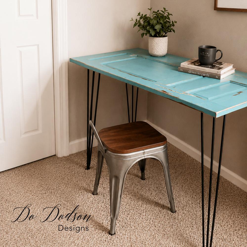Turquoise salvaged door on black hairpin legs used as a desk, with a metal chair, a potted plant and a coffee cup