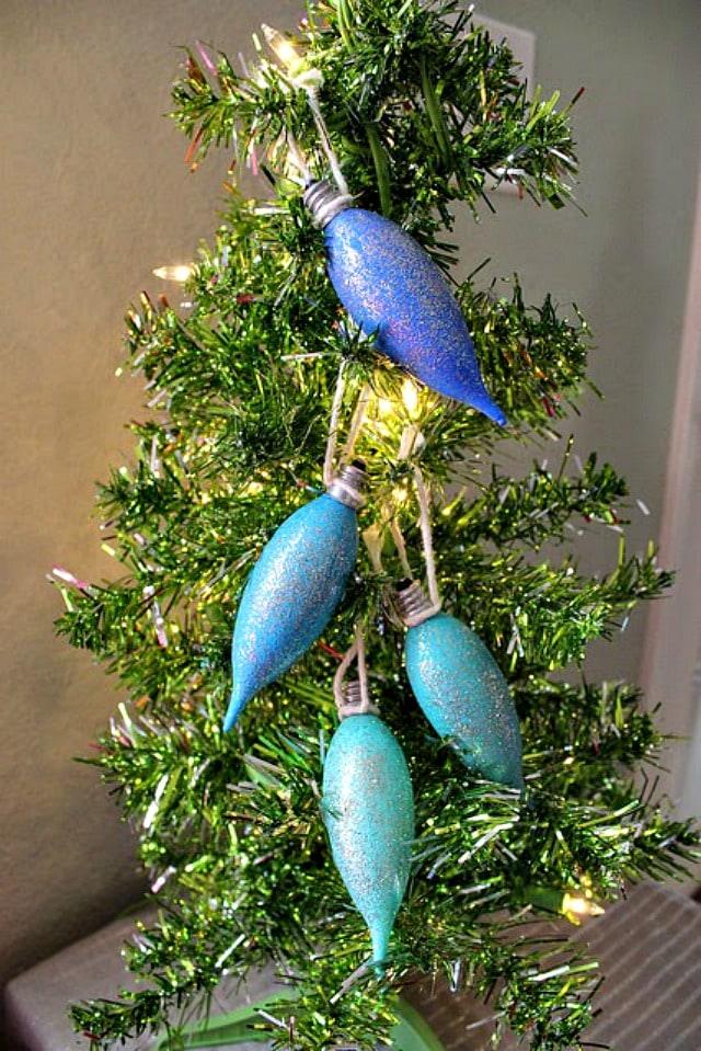 Burned out light bulbs painted in blended ombre colors hanging on a Christmas tree branch as ornaments