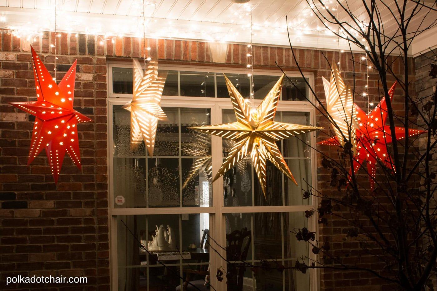 Red and gold paper star lanterns glowing under a brick porch ceiling strung with white lights beside a window at night