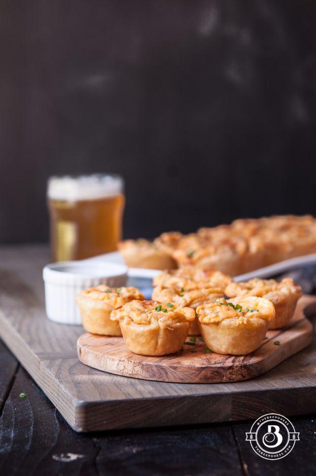 Buffalo beer cheese bites lined up on a dark wooden serving board with a tall glass of beer behind them