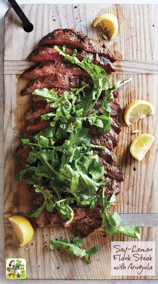 Sliced soy lemon flank steak fanned out across a wooden board over peppery arugula with halved lemons