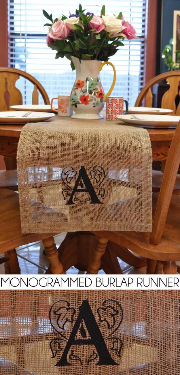 A frayed burlap table runner with a large stenciled black monogram stretches down a plain wooden dining table
