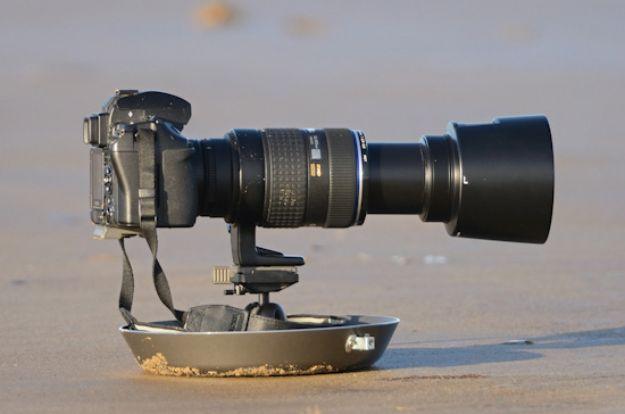 DIY ground pod, a DSLR with a long telephoto lens mounted on a shallow metal dish resting on open sand at the water line
