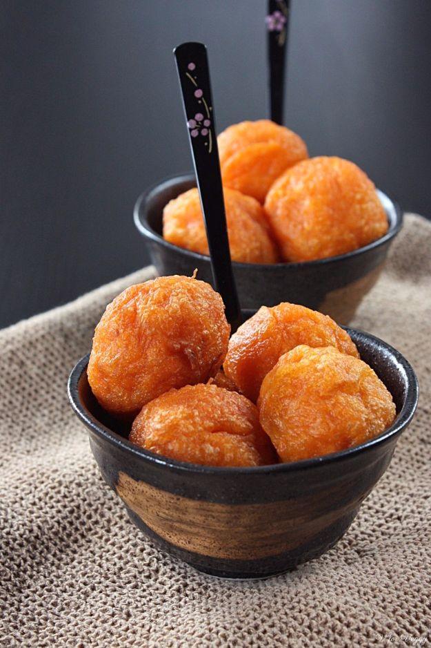 Deep fried orange sweet potato balls piled into two small black bowls with forks, sitting on burlap cloth