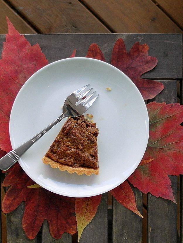 Slice of coffee pecan tart on a white plate with a fork, red autumn leaves on weathered grey wood behind