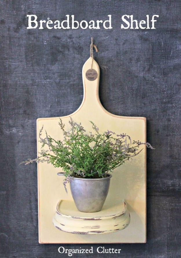 A vintage wooden breadboard mounted as a small wall shelf holds a tiny potted plant, two hooks screwed underneath