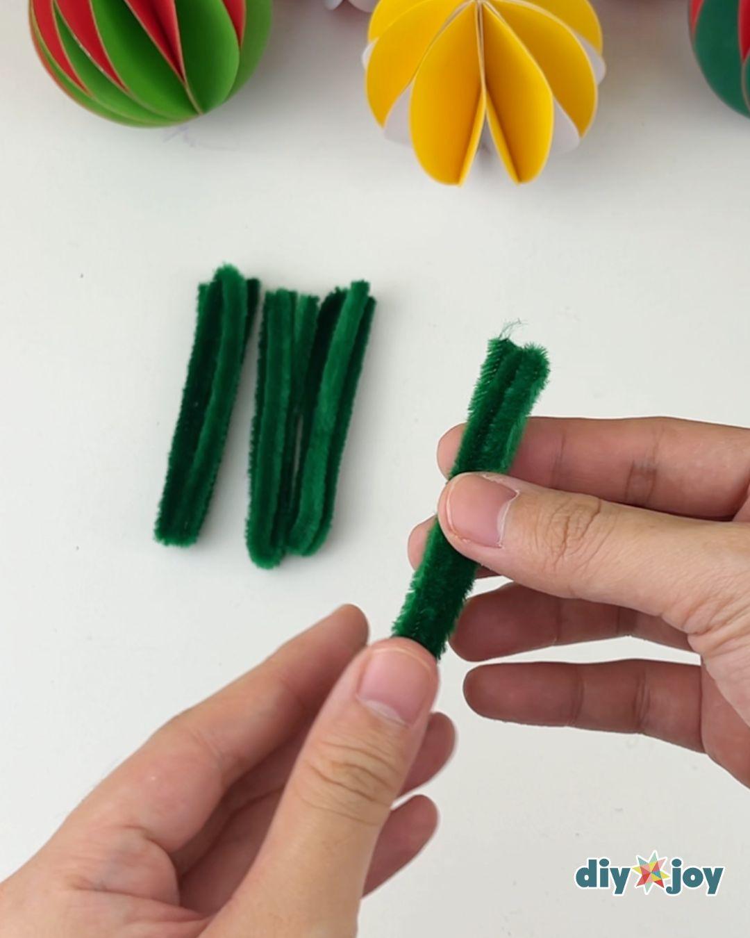 Easy Crafts - two hands fold a cut length of green pipe cleaner in half with three already folded pieces on the table beside them