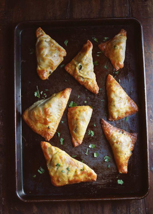 Low carb Indian vegetable samosas, golden triangles scattered on a dark baking sheet with fresh cilantro