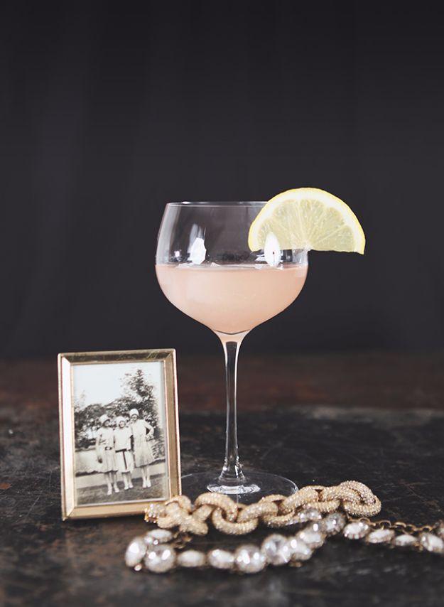 A coupe of pale Poor Liza cocktail with a lemon wedge on the rim, beside a vintage photo frame and pearls