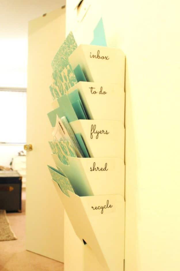 White wall mounted file rack with five slots labelled inbox, to do, flyers, shred and recycle, holding teal folders