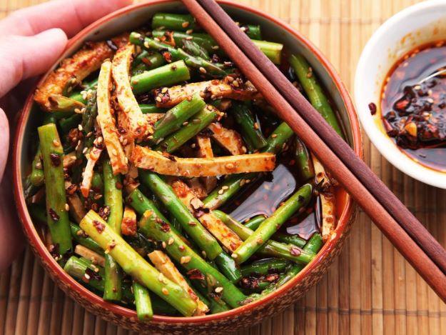 Sichuan asparagus and tofu salad in a bowl with cut asparagus, tofu strips and chili oil, chopsticks beside