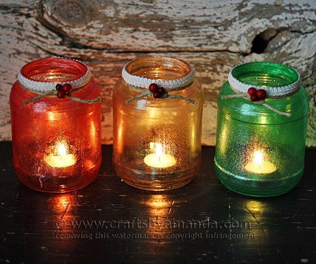 Three glitter jar luminaries in red, gold and green with lace trim and berries glowing with tea lights on a black table