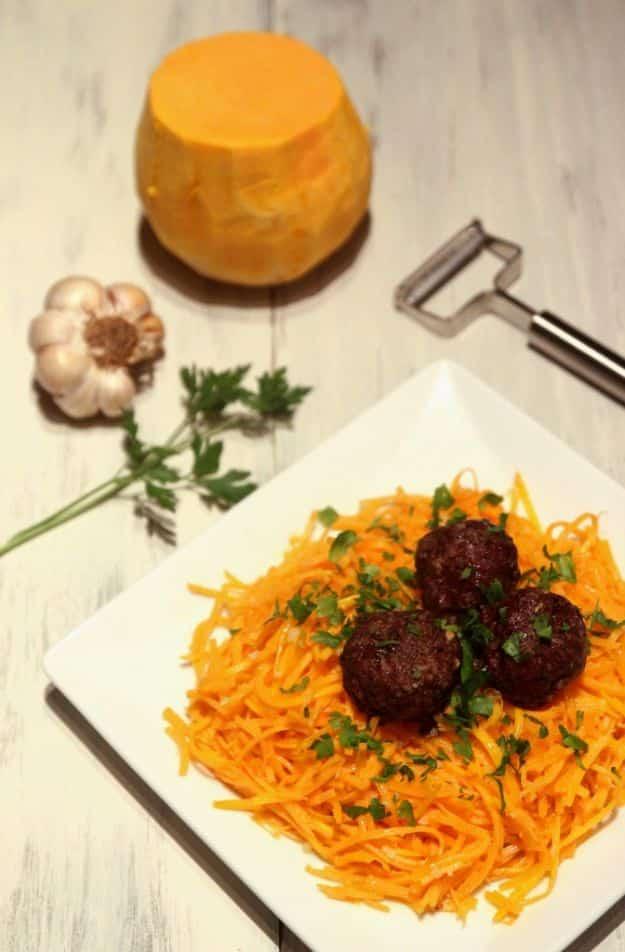 Butternut squash spaghetti noodles on a square plate topped with three dark browned meatballs and parsley