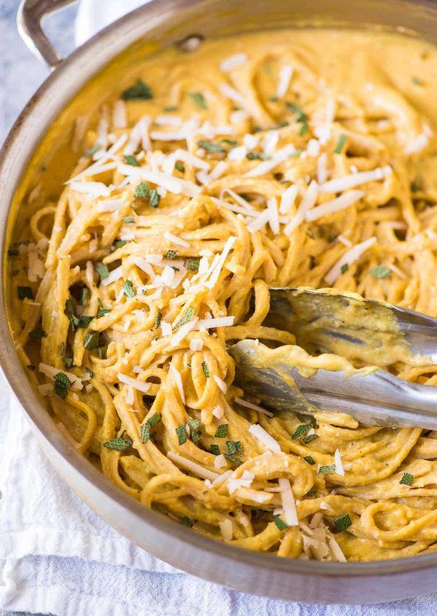 Wide pan of spaghetti coated in a creamy orange pumpkin sauce with parmesan, sage and metal serving tongs