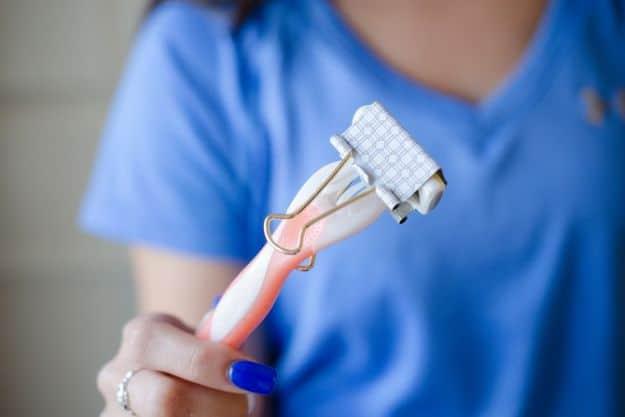 A hand holding a pink disposable razor with a silver binder clip fitted over the head to cover the blades