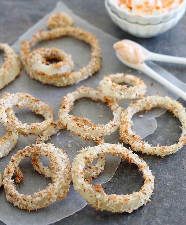 Coconut crusted baked onion rings cooling on parchment paper beside a small white bowl of coconut flakes