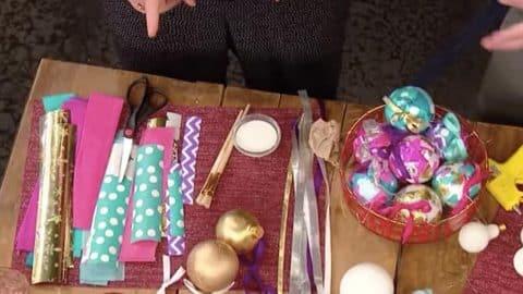 Leftover wrapping paper ornaments in progress with rolls of paper, scissors and a red bowl of finished balls