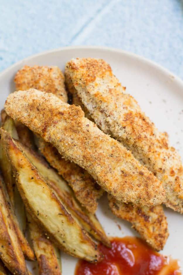 Clean eating baked chicken tenders, breaded golden tenders on a white plate with potato wedges and ketchup
