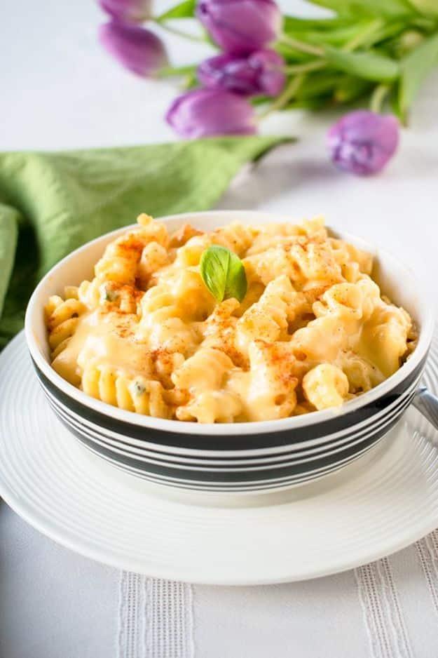 Italian mac and cheese in a black and white striped bowl on a white plate, with basil and purple tulips behind