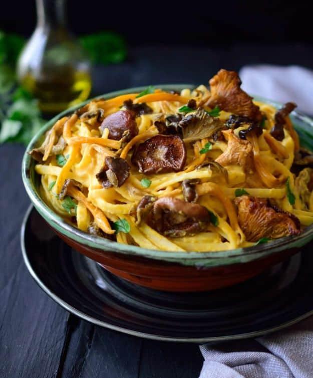 Vegan pumpkin pasta with wild mushrooms twirled in a green bowl on a dark table with a bottle of olive oil