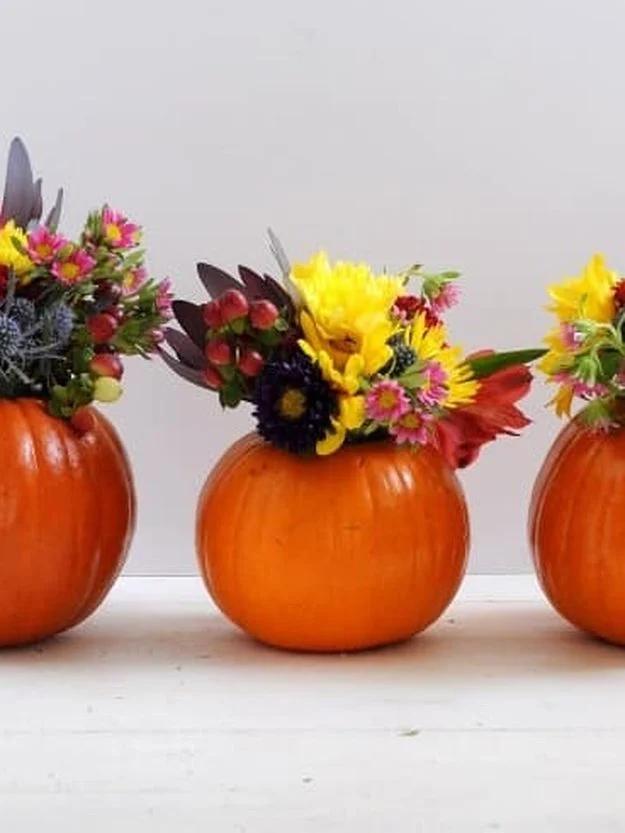 Three small orange pumpkins hollowed out into vases holding yellow, pink and purple fall flower posies