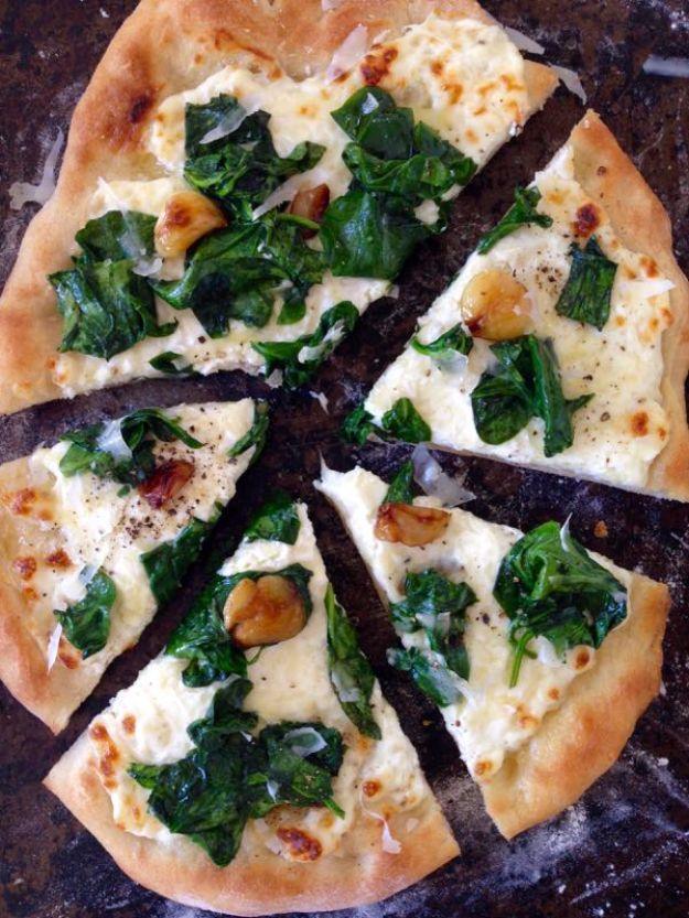 White pizza cut into slices topped with wilted spinach, roasted garlic cloves and melted ricotta and fontina