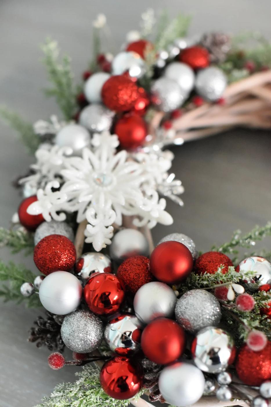A grapevine wreath packed with red and silver ball ornaments, white glitter snowflakes, frosted greenery and berries