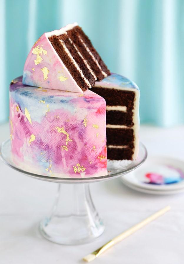 Watercolor graffiti chocolate cake with pink and blue washed frosting and gold leaf, cut open and sliced