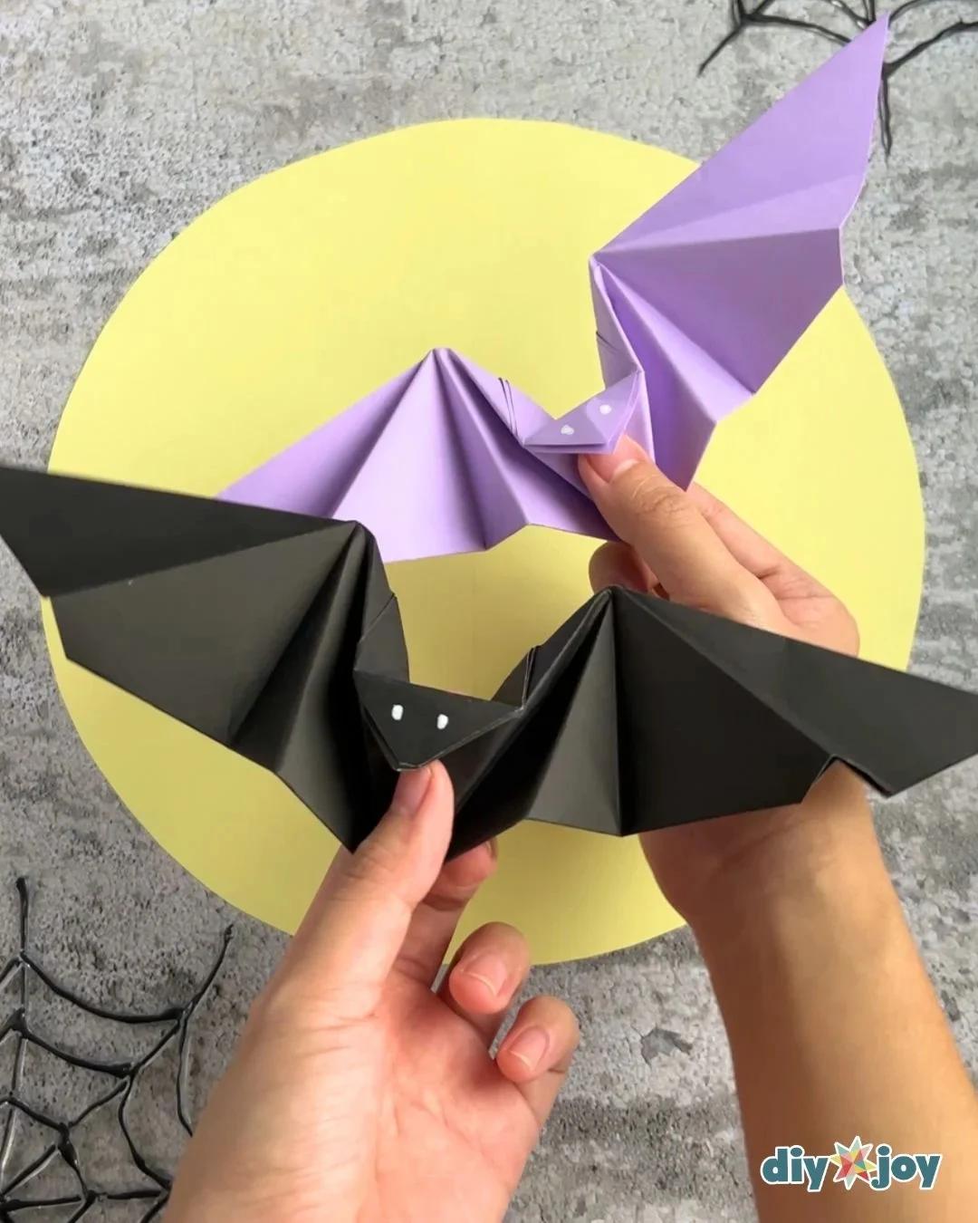 Halloween paper bats with flapping wings displayed on a table, each folded from a single square of paper.