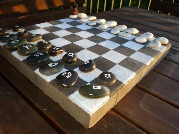 Concrete paver painted as a checkerboard on a wooden deck, set with dark and light pebble chess pieces