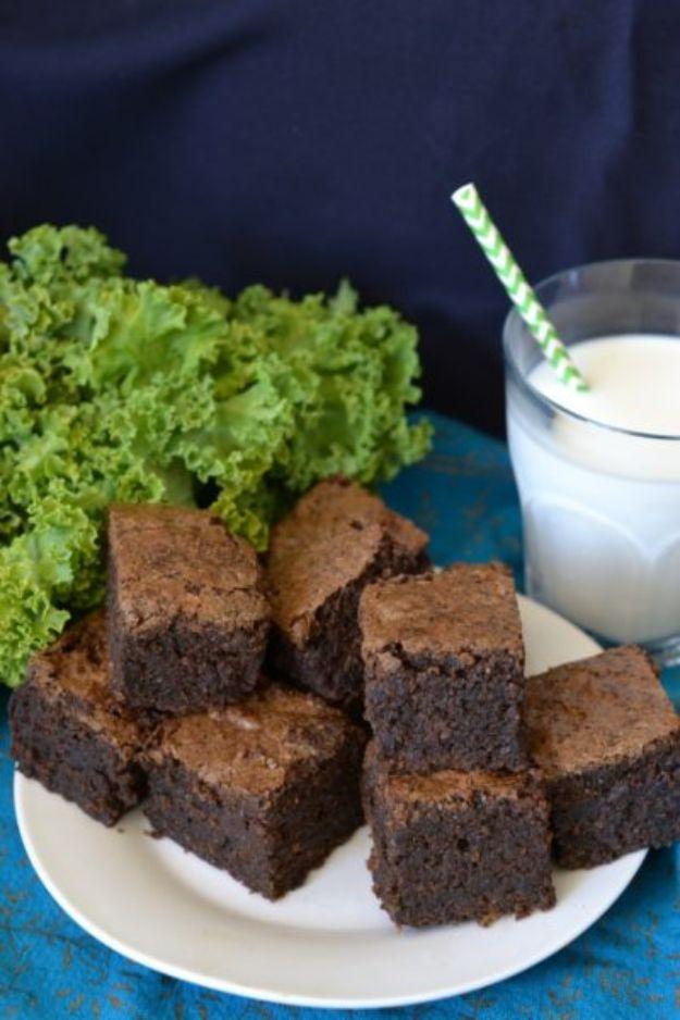 Kale brownies cut into squares on a white plate with fresh kale leaves and a glass of milk behind them