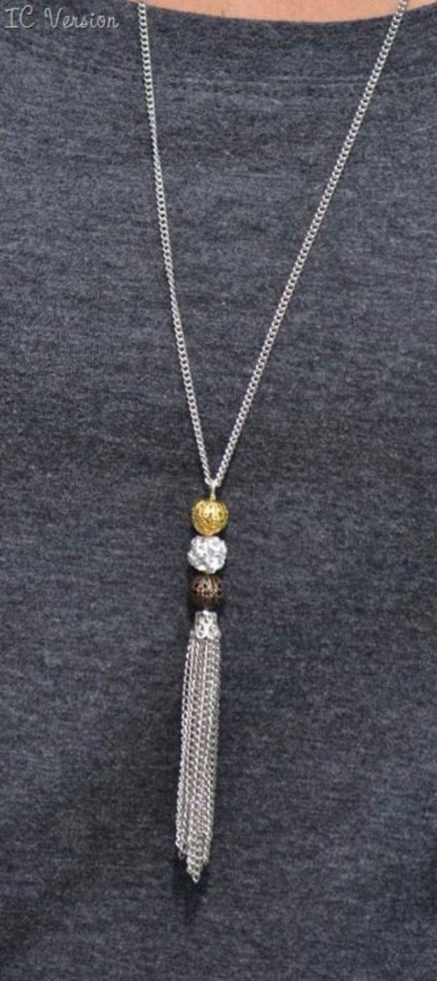 Mixed metal filigree ball necklace, a long silver chain with stacked metal beads over a fine chain tassel on a grey top