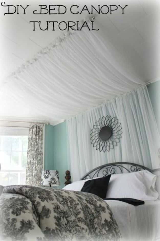 Bed canopy made from sheer white curtains hung from ceiling rods over a bed with gray floral bedding