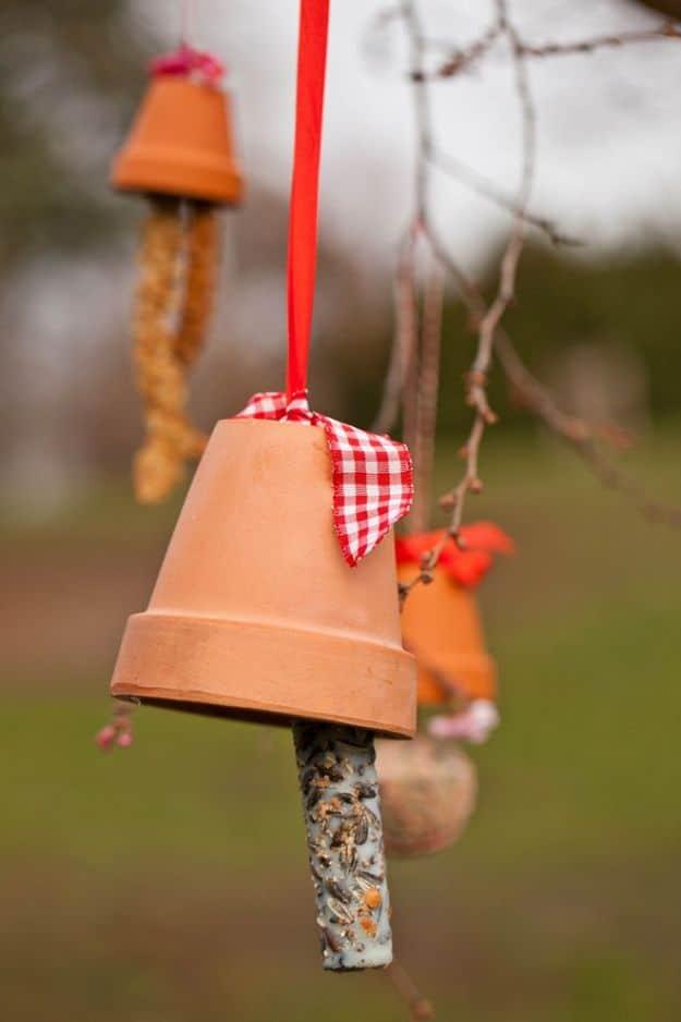 Terracotta clay pot bird feeder hung upside down on red ribbon with gingham bow, seed coated stick beneath as a perch